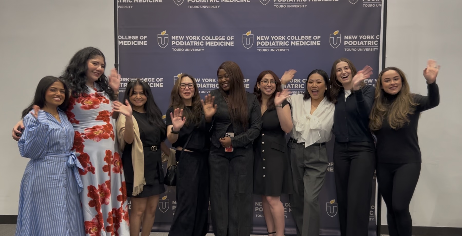 A group of students cheers in front of a NYCPM banner. 