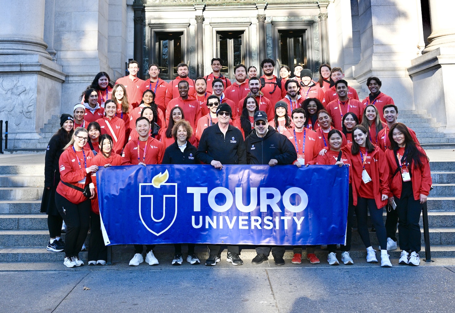 Students at New York College of Podiatric Medicine stand with university administration members while holding a university banner.