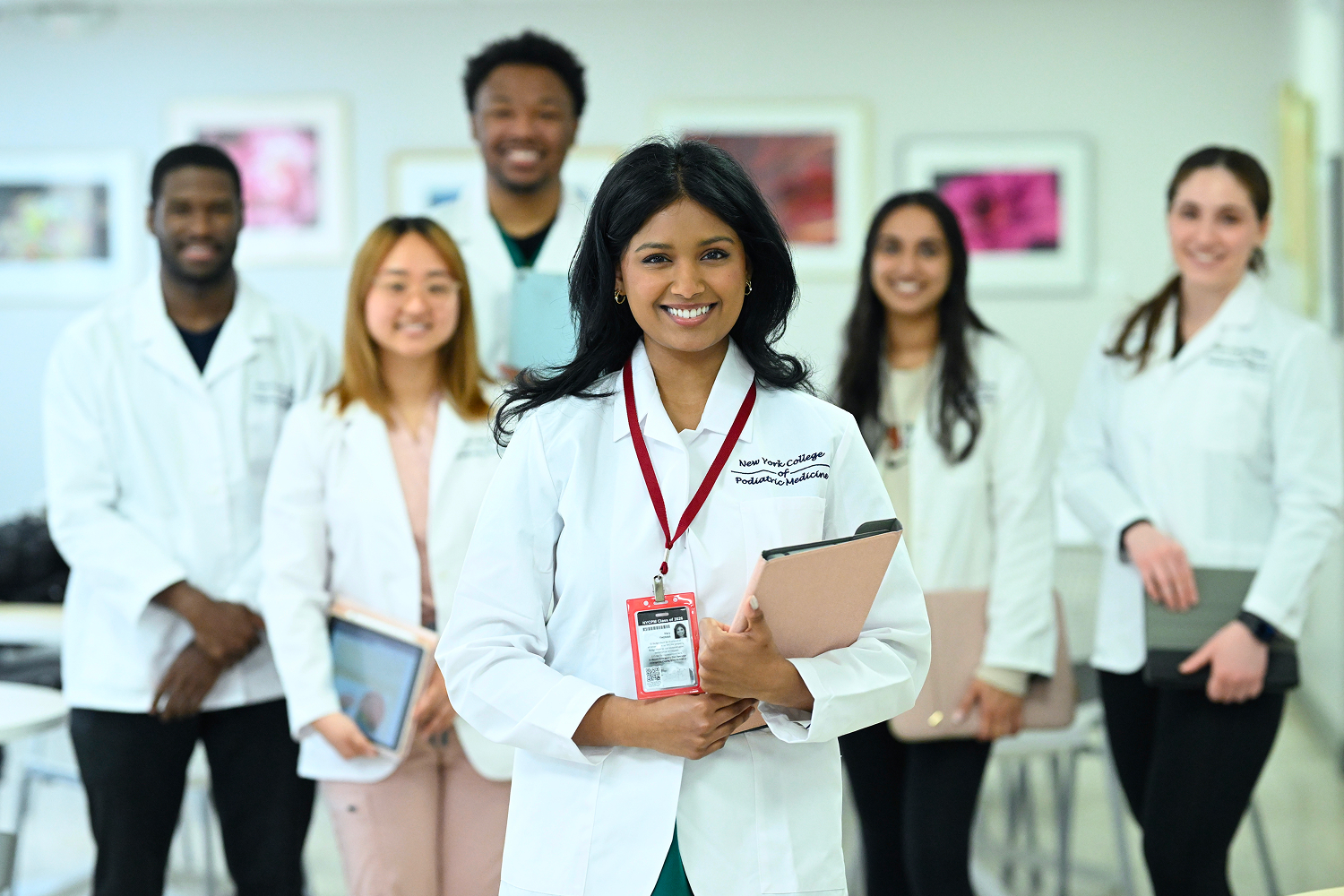 Group of students smiling while wearing scrubs in classroom