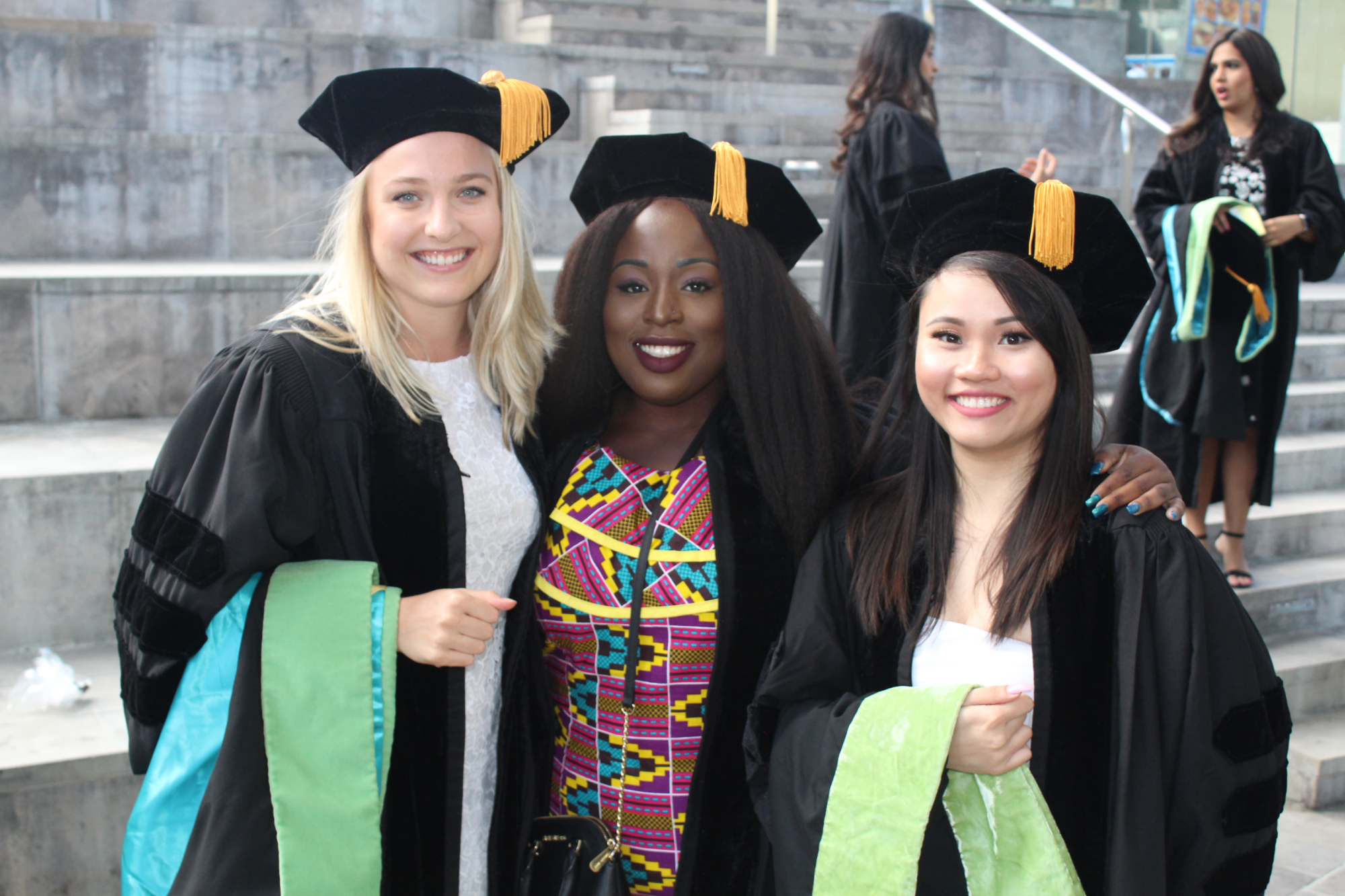 Three NYCPM grads in regalia at commencement