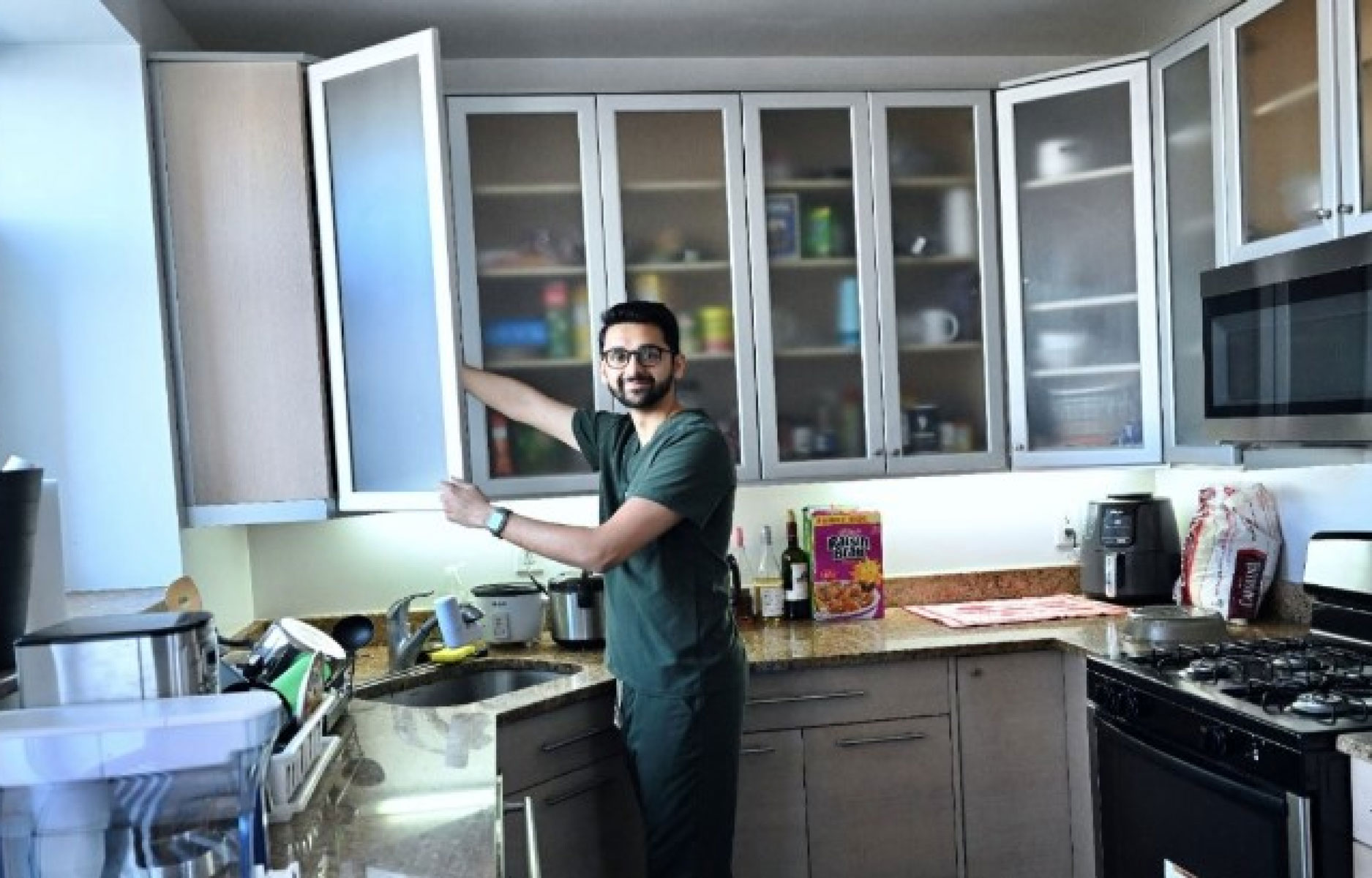 Student smiling while reaching into kitchen cabinet