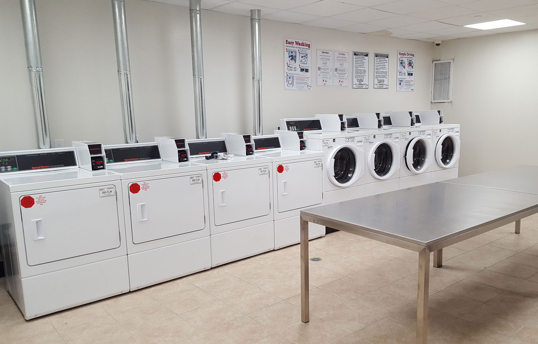 Laundry room with a row of washers and dryers, and a table for folding clothes